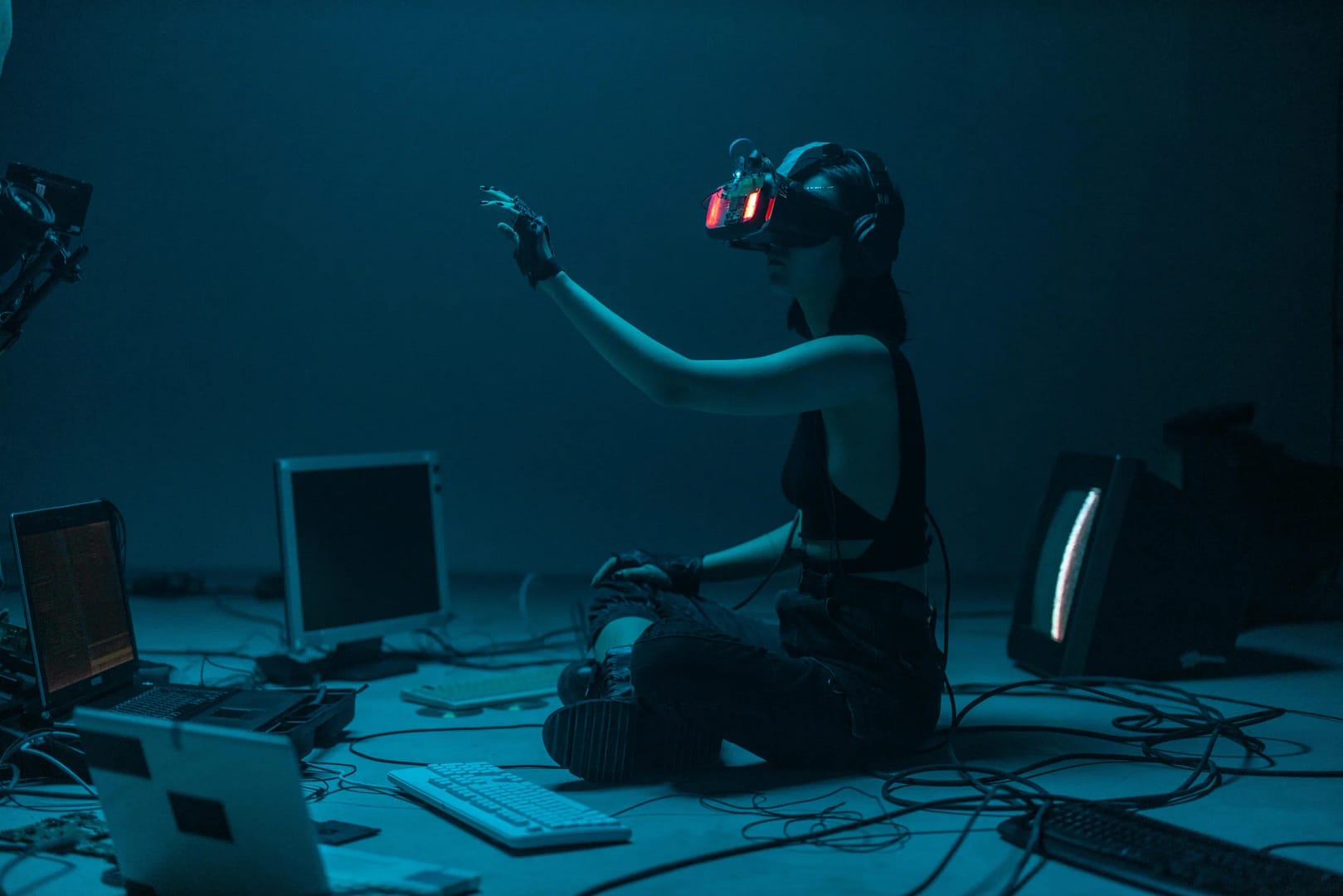 Photograph of a young woman in a darkened room wearing a VR headset, surrounded by laptops, illustrating legal rights in the metaverse.