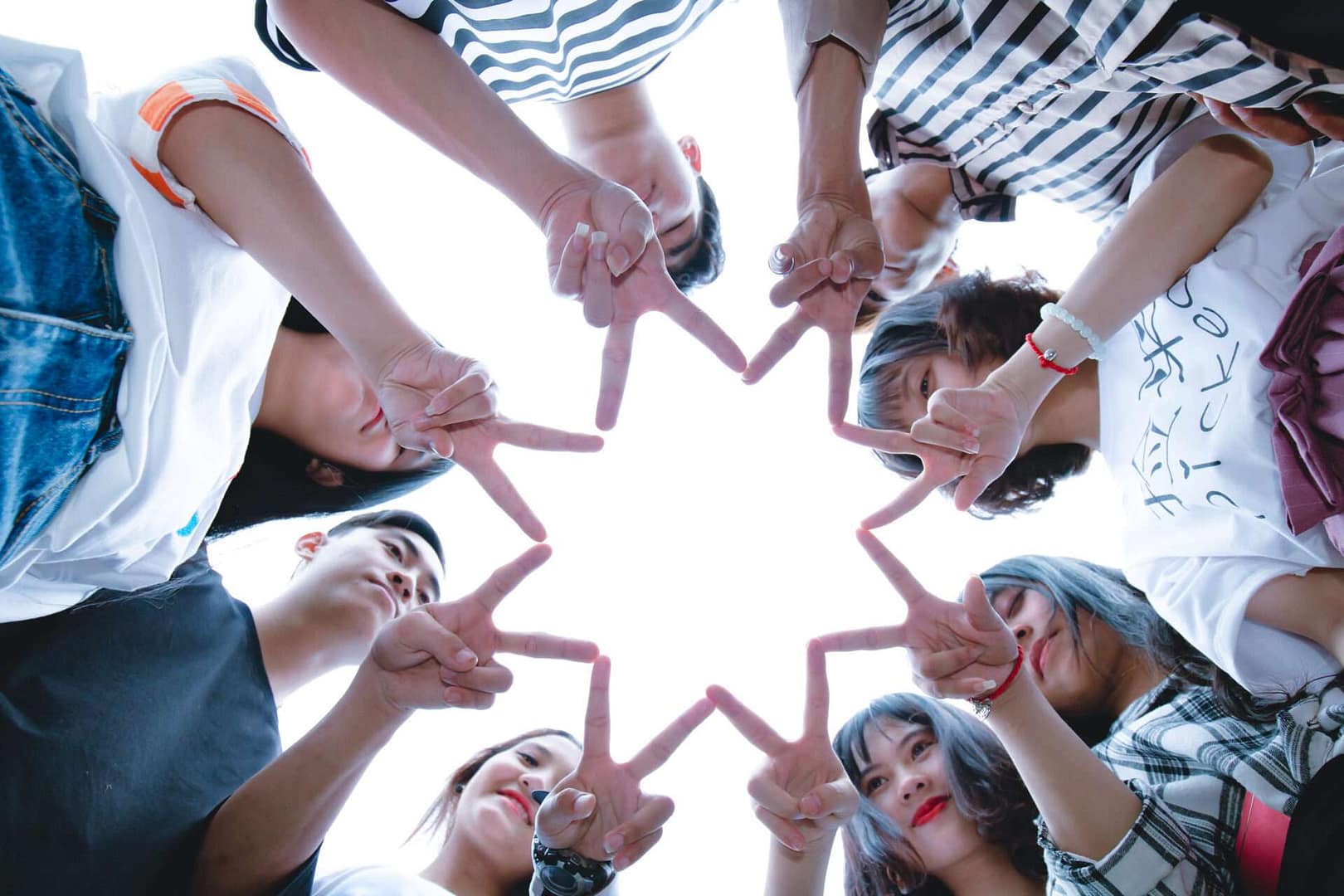 Group of young people standing in a circle many a collective star with their fingers