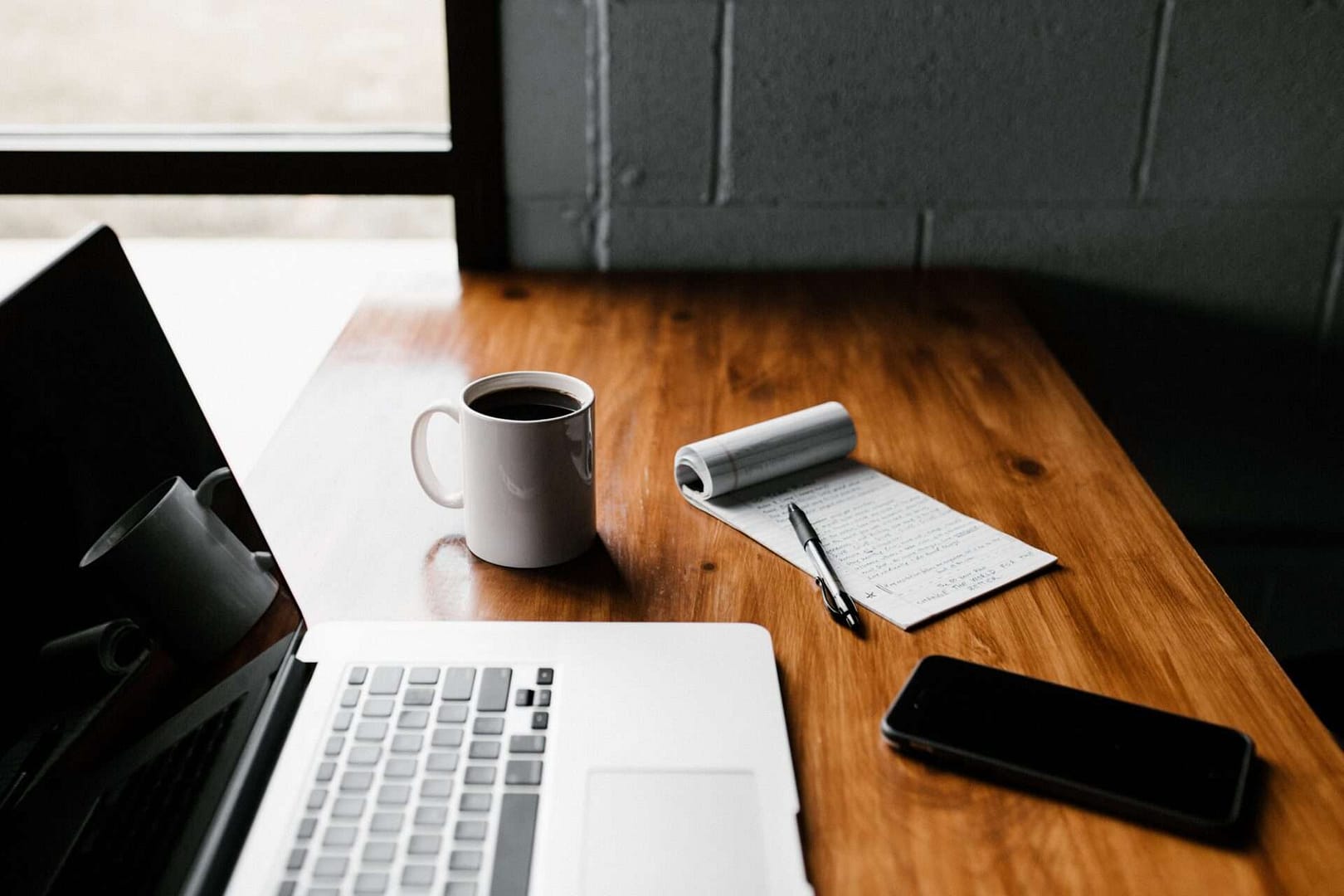photograph of a desk with a coffee, laptop, notebook and pen to illustrate the power of self-discipline
